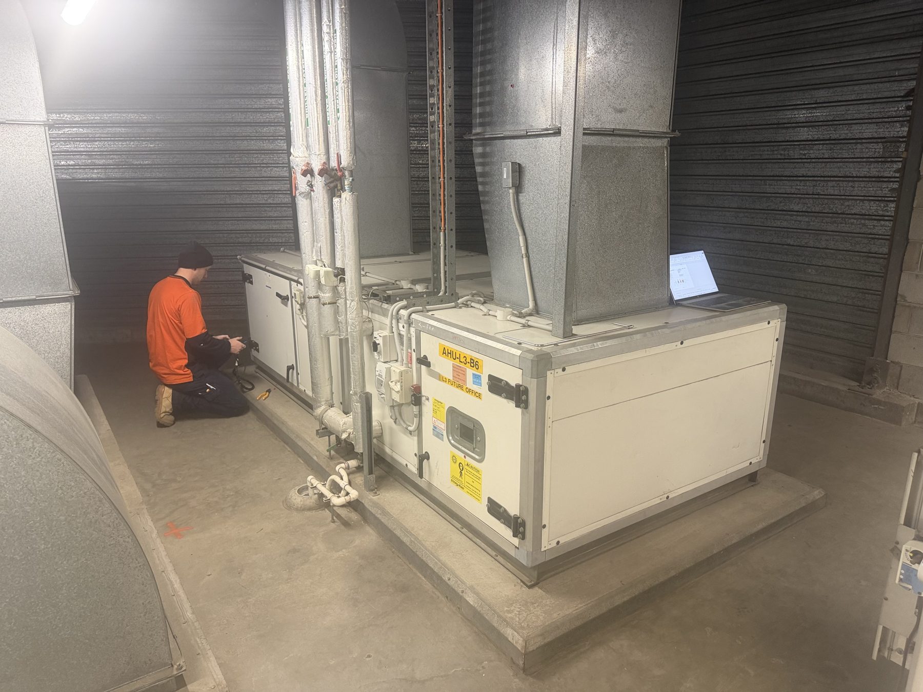 Technician servicing a packaged air handling unit in a basement plant room